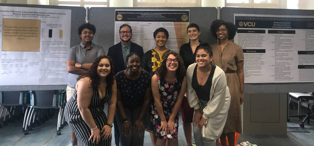 Group of nine students in front of a backdrop of research posters
